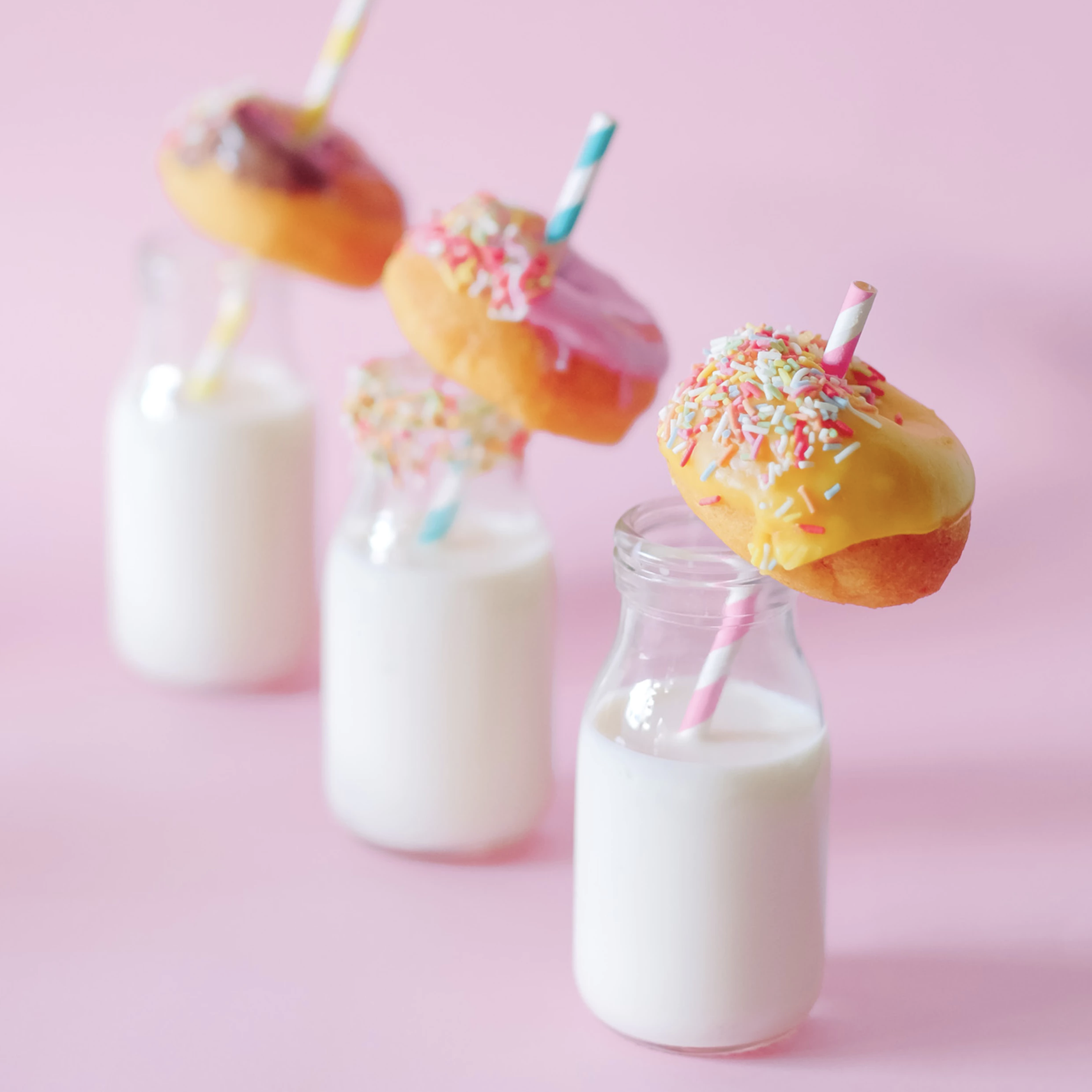 Three small milk jugs with a blue and pink colored straw with a donut inside the straw